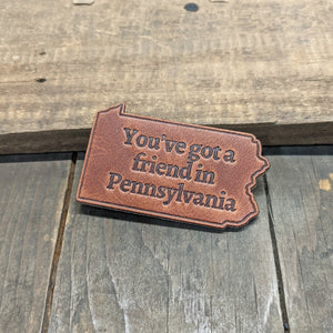 A tan piece of leather in the shape of the state of pennsylvania, embossed with the text "You've got a friend in Pennsylvania".
