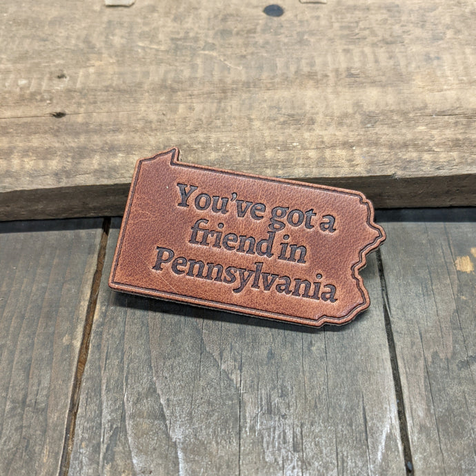 A tan piece of leather in the shape of the state of pennsylvania, embossed with the text 